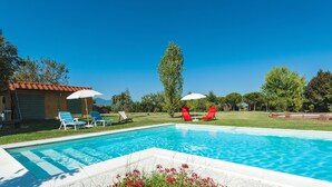 Una piscina con sillas de descanso, una zona de estar cubierta y un césped bien cuidado.