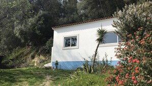 A white building with a red-tiled roof, surrounded by greenery and a dirt path.