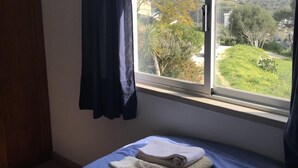 A bedroom with a bed, a window with a view of a green landscape, and a curtain.