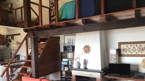 A cozy living room with a wooden staircase, a fireplace, a bookshelf, and a television.