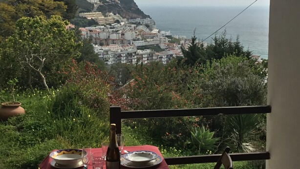 A table set with plates and a bottle, overlooking a coastal town with buildings on a hillside.