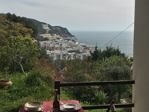 A table set with plates and a bottle, overlooking a coastal town with buildings on a hillside.