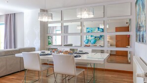 Ein moderner Essbereich mit einem Glastisch, weißen Stühlen und einer Chandelüster.