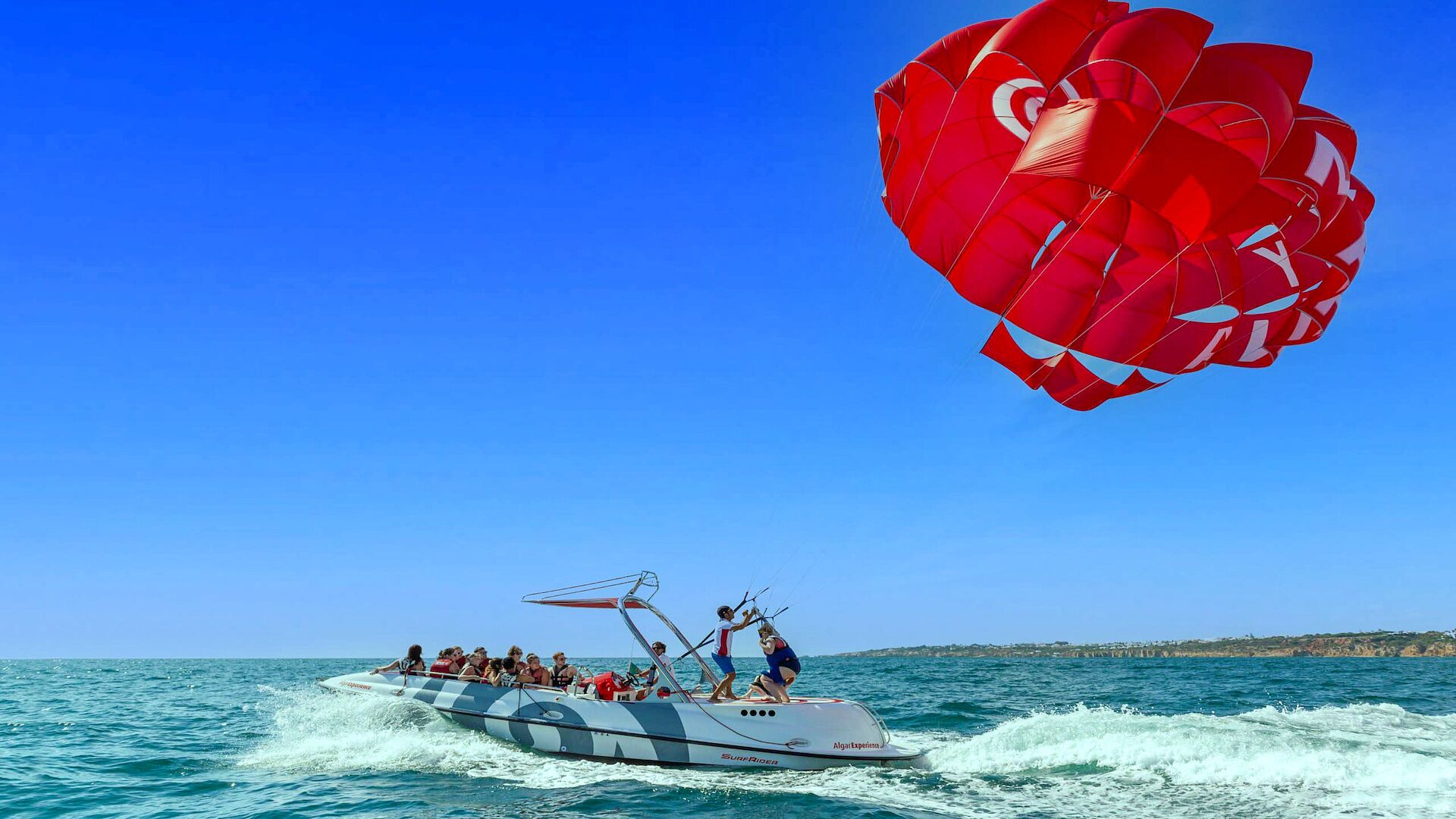 Una embarcación con pasajeros y un parasail al fondo.