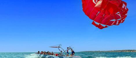 Una embarcación con pasajeros y un parasail al fondo.
