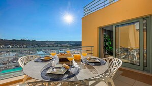 Ein runder Tisch mit Blick auf einen Yachthafen und Stadtpanorama, gedeckt mit Tellern, Gläsern und einer Karaffe Orangensaft.