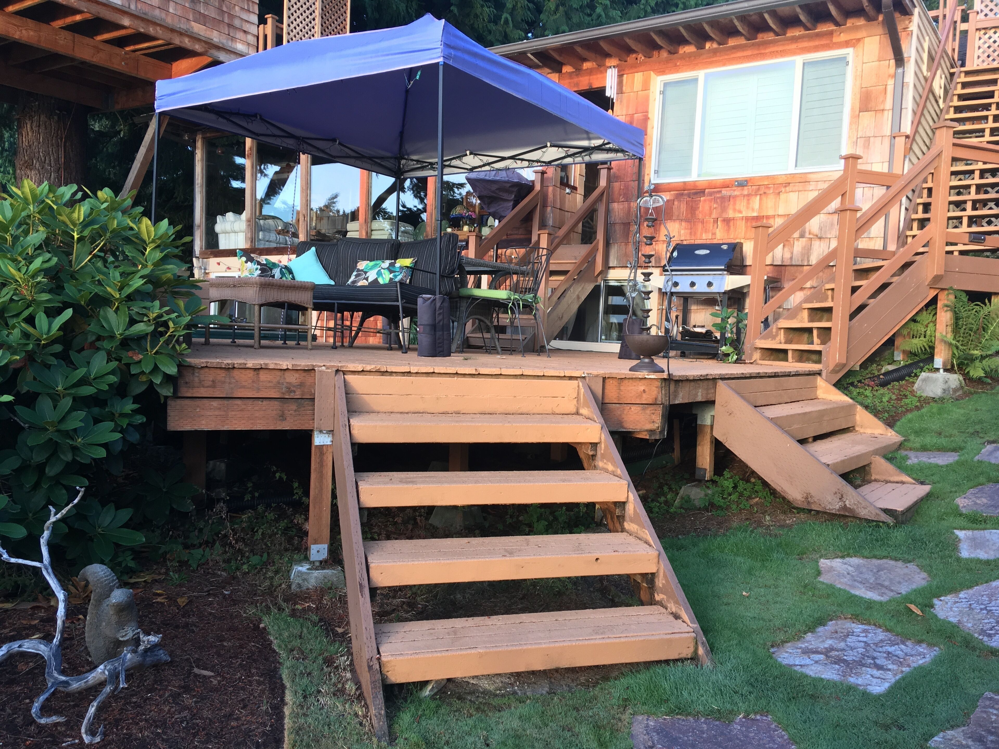 Eine Holzterrasse mit Gartenmöbeln, einem Grill und einer überdachten Sitzgelegenheit.