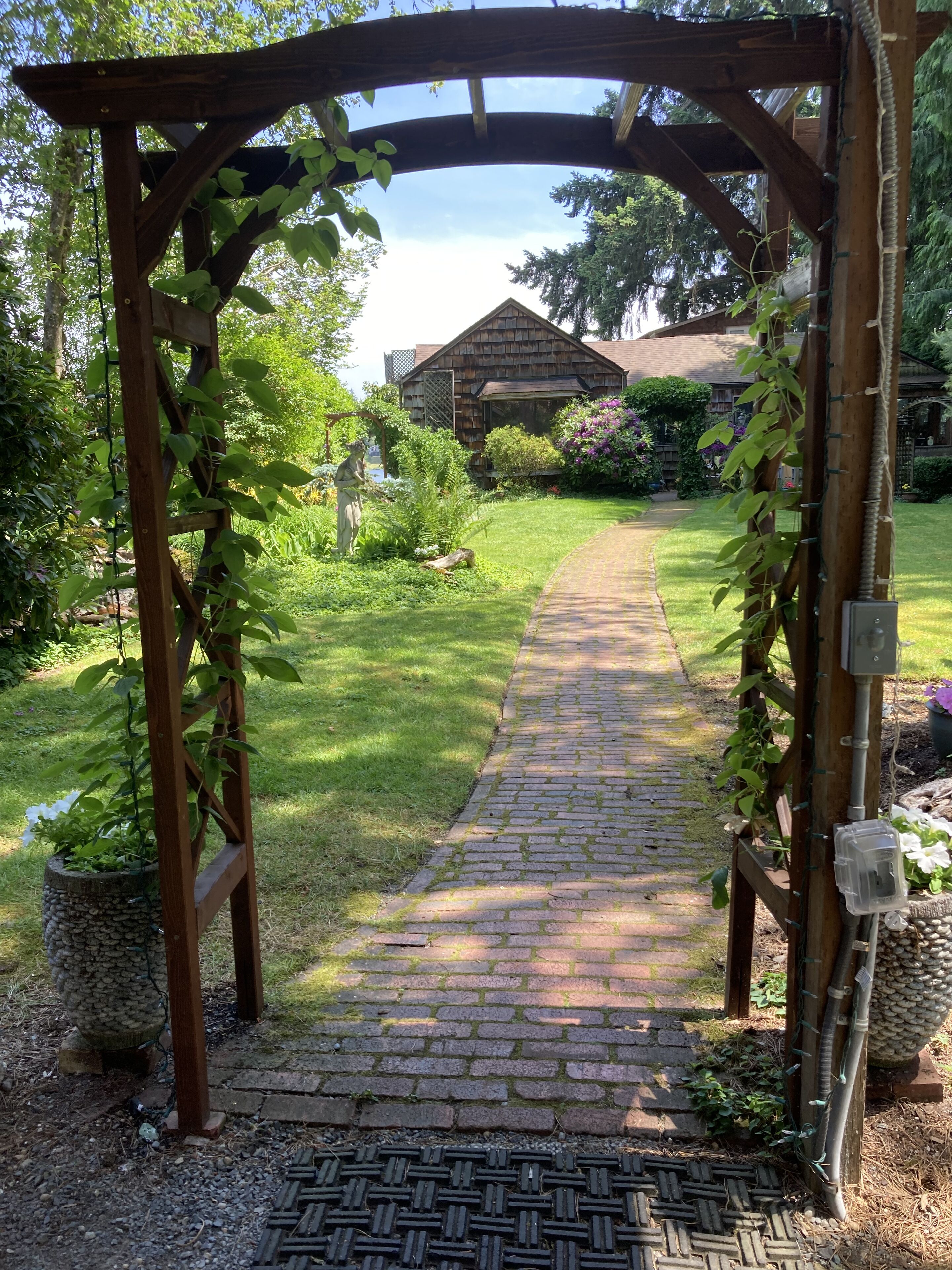 A brick pathway leading to a wooden pergola with climbing plants.