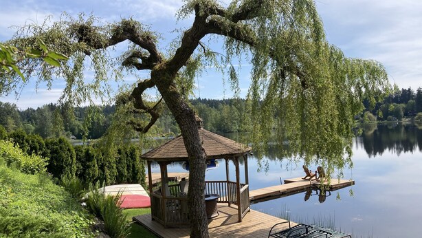 A gazebo with a wooden deck overlooking a calm lake, surrounded by lush greenery and a clear sky. - Cottage Lake Bed and Breakfast (Woodinville)