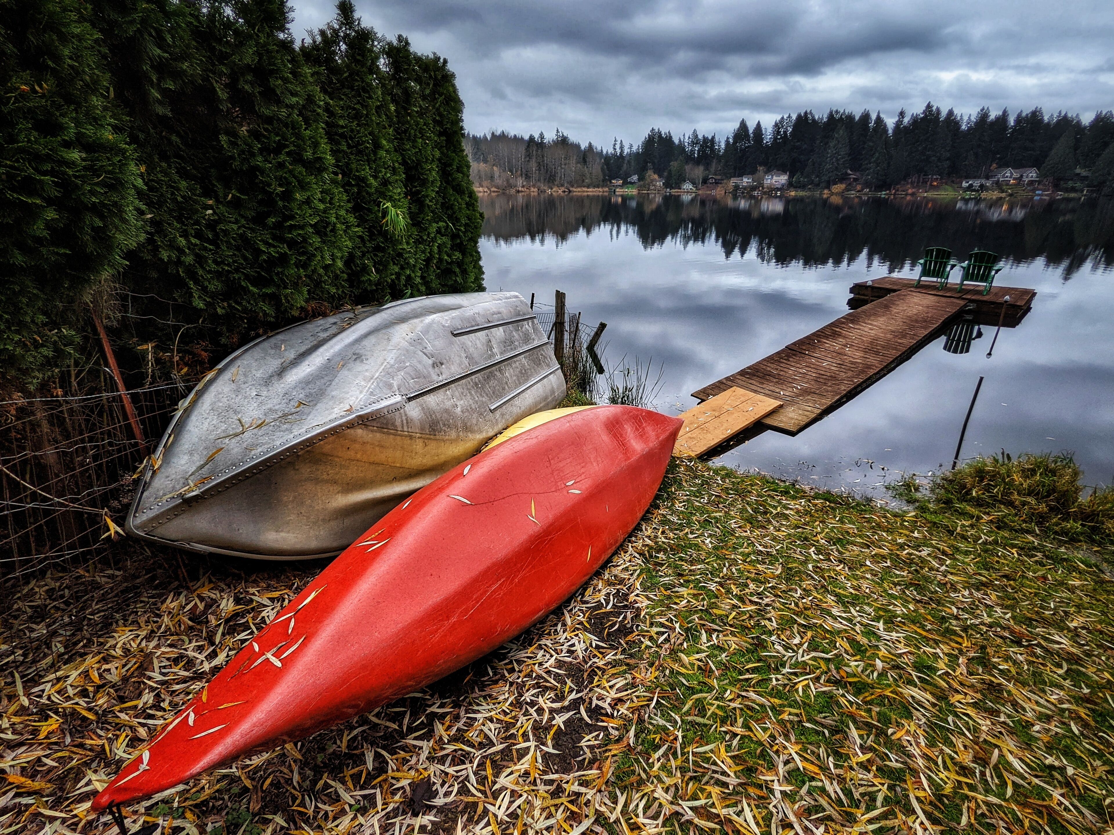 A kayak and canoe resting on a dock by a calm lake with a forest backdrop.