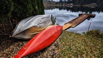 A kayak and canoe resting on a dock by a calm lake with a forest backdrop.