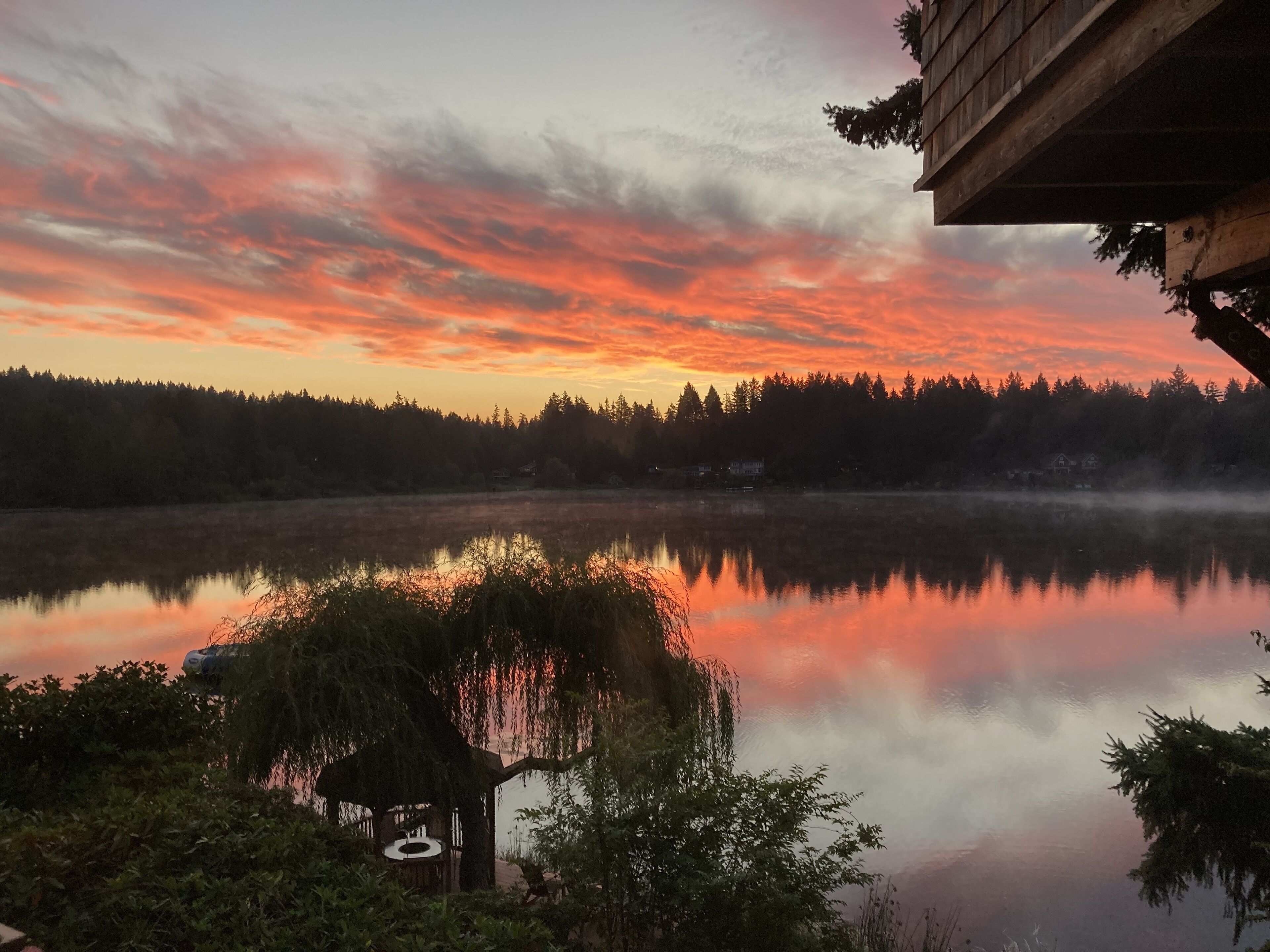 A serene lakeside view with a wooden cabin and a gazebo reflecting the sunset.
