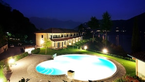 A well-lit swimming pool area with a house in the background.