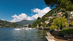 A waterfront with boats docked, a walking path, and buildings on a hillside.