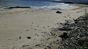 A beach with a rocky shoreline, calm sea, and distant mountains under a partly cloudy sky.