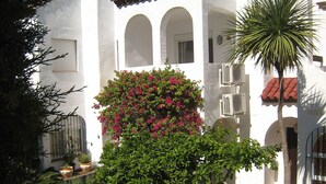 A white building with arched windows and a tiled roof, surrounded by greenery and potted plants. - TOWN HOUSE IN SECURE  URBANIZATION.   AIR CON.   INTERNET.   MOSQUITO SCREENS. (ESTEPONA)