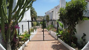 A gated courtyard with a paved walkway, surrounded by white walls and various plants. - TOWN HOUSE IN SECURE  URBANIZATION.   AIR CON.   INTERNET.   MOSQUITO SCREENS. (ESTEPONA)