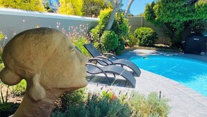 A swimming pool with lounge chairs, surrounded by greenery and a mushroom sculpture. - Luxurious self-catering cottage sleeping up to 4 adults (Cape Town)