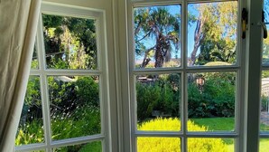 A bay window with multiple panes, offering a view of a well-maintained garden with various plants and trees. - Luxurious self-catering cottage sleeping up to 4 adults (Cape Town)