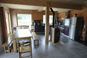 A spacious kitchen with modern appliances, a dining area with a wooden table and chairs, and a view of the outdoors through large windows.
