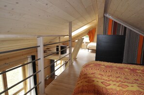 A loft-style bedroom with a bunk bed, a desk, and a large bed with patterned bedding.