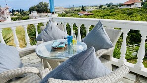 Ein Balkon mit Korbstühlen und Kissen, einem Glastisch mit Flasche und Glas sowie Blick auf die umliegende Landschaft.