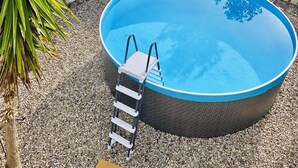 Ein runder Pool im Freien mit einer Leiter, umgeben von Kies und verschiedenen Pflanzen.