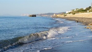 A beach with waves, a rocky shoreline, and buildings in the background.