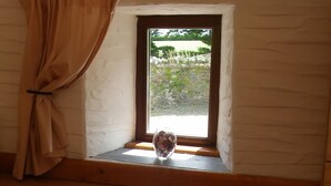 A window with a curtain, a small window sill, and a clear view of an outdoor garden. - Beautifully Renovated Stable & Cart House | Peaceful West Wales Farm Stay (Hebron)