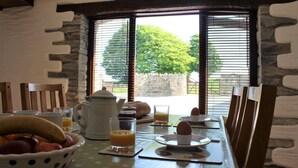 A breakfast table set with a fruit bowl, coffee, juice, and pastries, overlooking a stone wall and greenery. - Beautifully Renovated Stable & Cart House | Peaceful West Wales Farm Stay (Hebron)