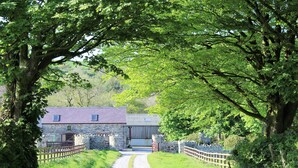 A stone building with a metal roof, a gravel path leading to it, and a wooden fence. - Beautifully Renovated Stable & Cart House | Peaceful West Wales Farm Stay (Hebron)