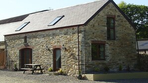 A stone building with a sloped roof, two skylights, and a wooden bench outside. - Beautifully Renovated Stable & Cart House | Peaceful West Wales Farm Stay (Hebron)