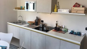 A modern kitchen with a stainless steel sink, a built-in oven, and a compact stove. There are shelves above the counter holding various kitchen items and a sign that reads "SUNDAY SEAT". - Suite Apartment Cavour- Exclusive"SunTripSicily" (Riposto)