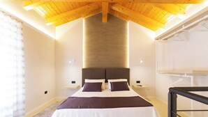 A bedroom with a high ceiling, a bed with white and dark bedding, two bedside tables, and a nightstand. - Suite Apartment Cavour- Exclusive"SunTripSicily" (Riposto)