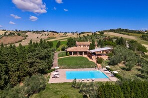 Eine Villa mit Swimmingpool, umgeben von üppiger Vegetation und sanften Hügeln.