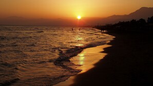 A beach at sunset with waves, a clear sky, and distant mountains.