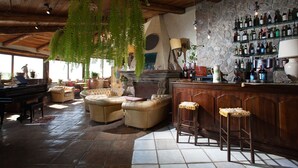 A rustic bar area with wooden furniture, a stone wall, and a variety of bottles.
