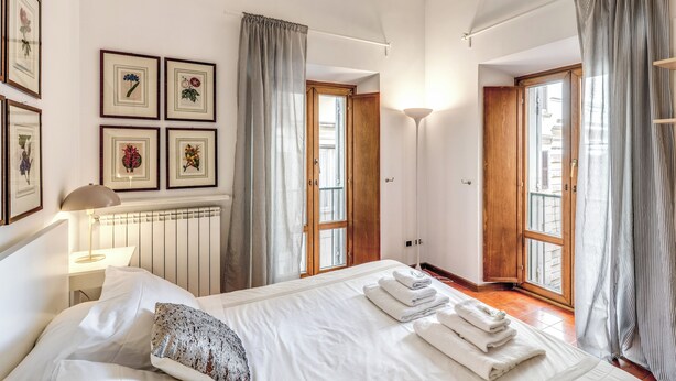 A bedroom with a large bed, a bedside table with a lamp, a radiator, and framed pictures on the wall. - 3 Bdr. Apt. Near Piazza Navona | 4 AC, WiFi, Heat (Roma)