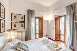 A bedroom with a large bed, a bedside table with a lamp, a radiator, and framed pictures on the wall. - 3-Bedroom Apartment Near Piazza Navona | 4 Air Conditioners, Wi-Fi, Heating (Roma)
