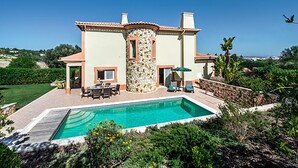 Une maison à deux étages dotée d’une piscine, de mobilier d’extérieur et d’une façade en pierre.