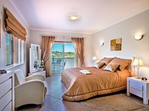 Une chambre à coucher avec un grand lit, un bureau, une chaise, une table de chevet et une vue sur l’extérieur.