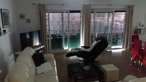 A living room with a sofa, a TV, a coffee table, and a chair. There are large windows with blinds. - Apartment with stunning sea views (Podgora)