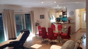 A modern living room with a glass dining table, red chairs, and a sofa. There is a kitchen area with a microwave and a clock on the wall. - Apartment with stunning sea views (Podgora)