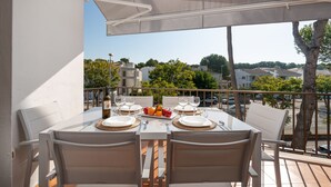 Un coin repas avec une table dressée pour deux personnes, des chaises d’extérieur et une vue sur le quartier environnant.