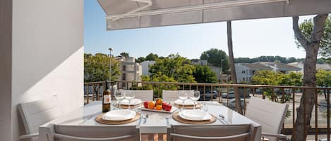 A dining area with a table set for two, outdoor chairs, and a view of the surrounding neighborhood.