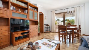 Un salon équipé d’un téléviseur, de bibliothèques en bois, d’une table à manger avec des chaises et offrant une vue sur l’extérieur.