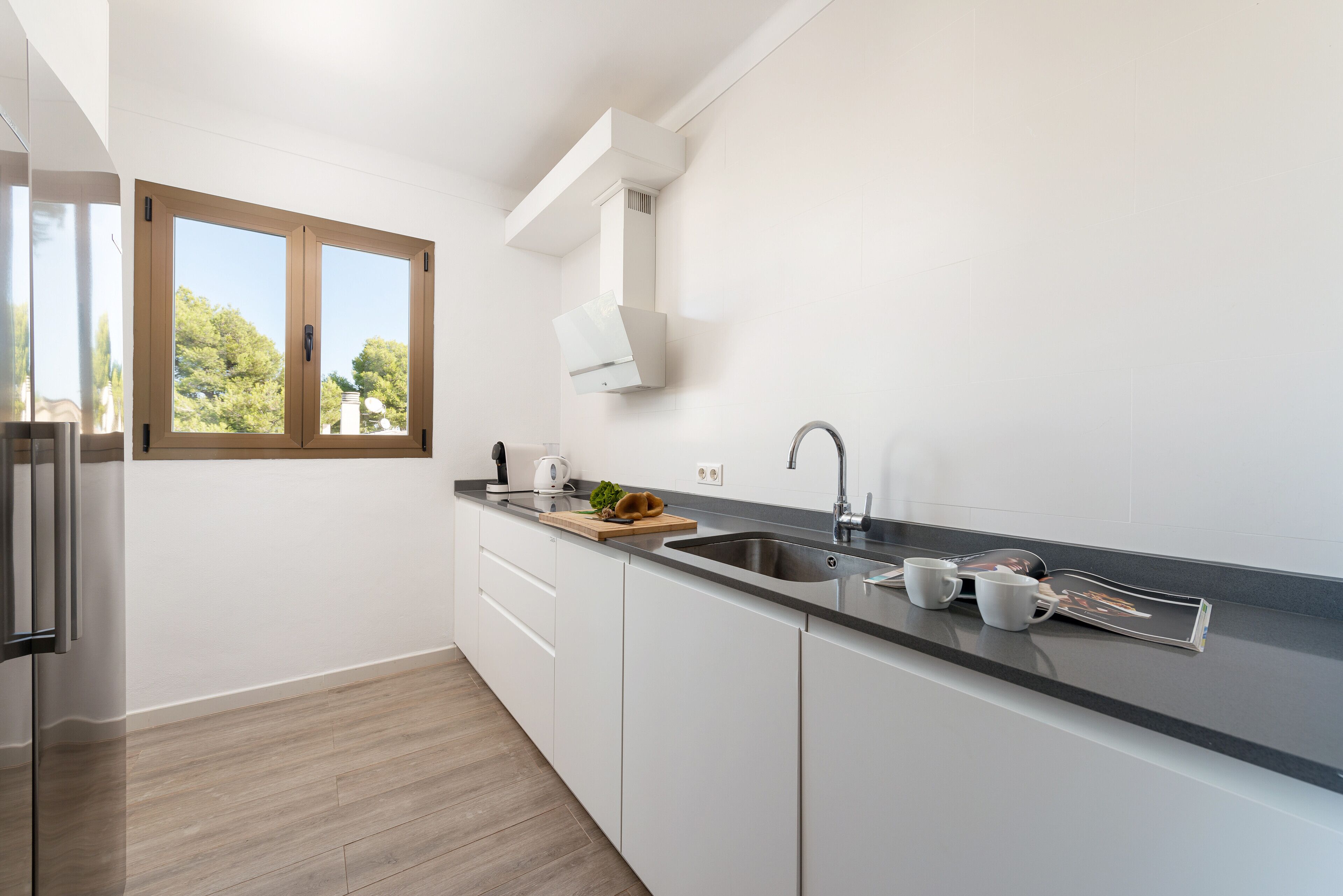 Una cocina moderna con armarios blancos, un lavamanos de acero inoxidable y una ventana con vistas a zonas verdes.
