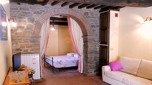 A bedroom with a stone archway, a bed with a canopy, a white sofa, and a small table with a decorative bowl. - Typical Tuscan style apartment (cortona)