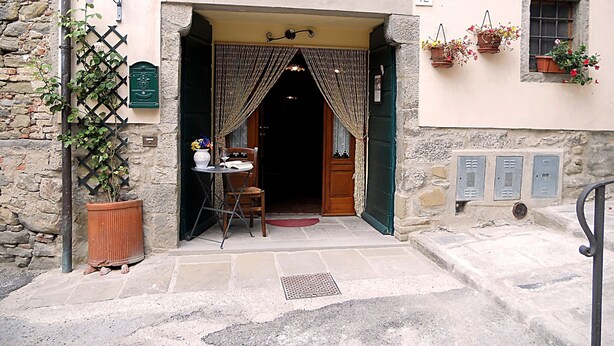 A stone building with a wooden door, a small table with a chair, and potted plants. - Typical Tuscan style apartment (cortona)