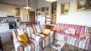 A cozy living room with striped sofas, a dining table, and a kitchen area. - VILLETTA BEL GIARDINO (MARINA DI CAMPO)